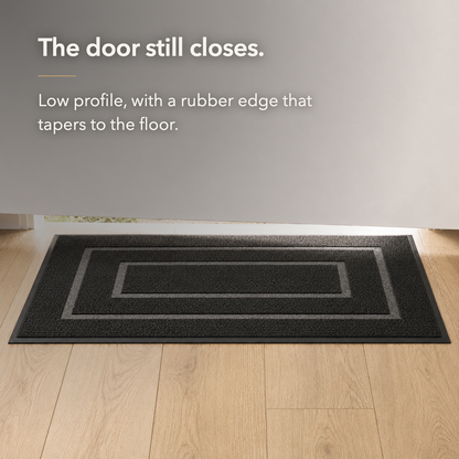 Black door mat seen from floor level at the foot of a door, showing how low the mat sits against the floor.