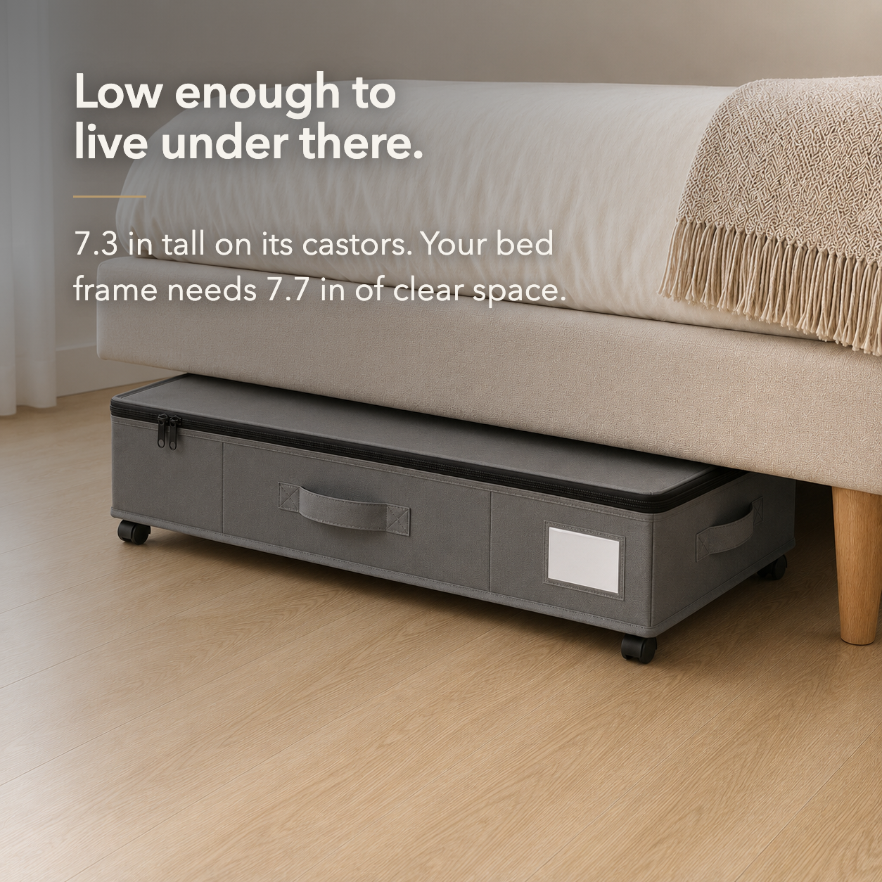 The grey under bed storage box tucked under an upholstered bed frame, with only a narrow gap above its closed lid