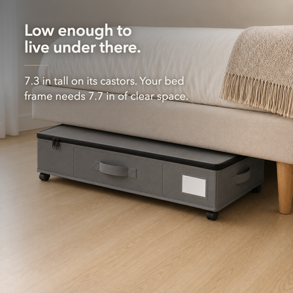The grey under bed storage box tucked under an upholstered bed frame, with only a narrow gap above its closed lid