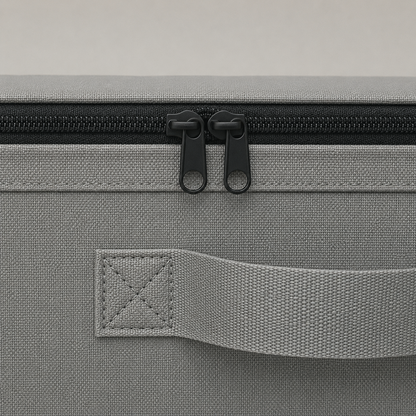 Close-up of the zipper and its twin pulls along the top rail, with a webbing side handle stitched to the gray fabric below.