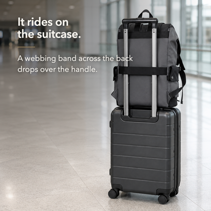 The backpack's rear webbing band dropped over the extended handle of a wheeled suitcase