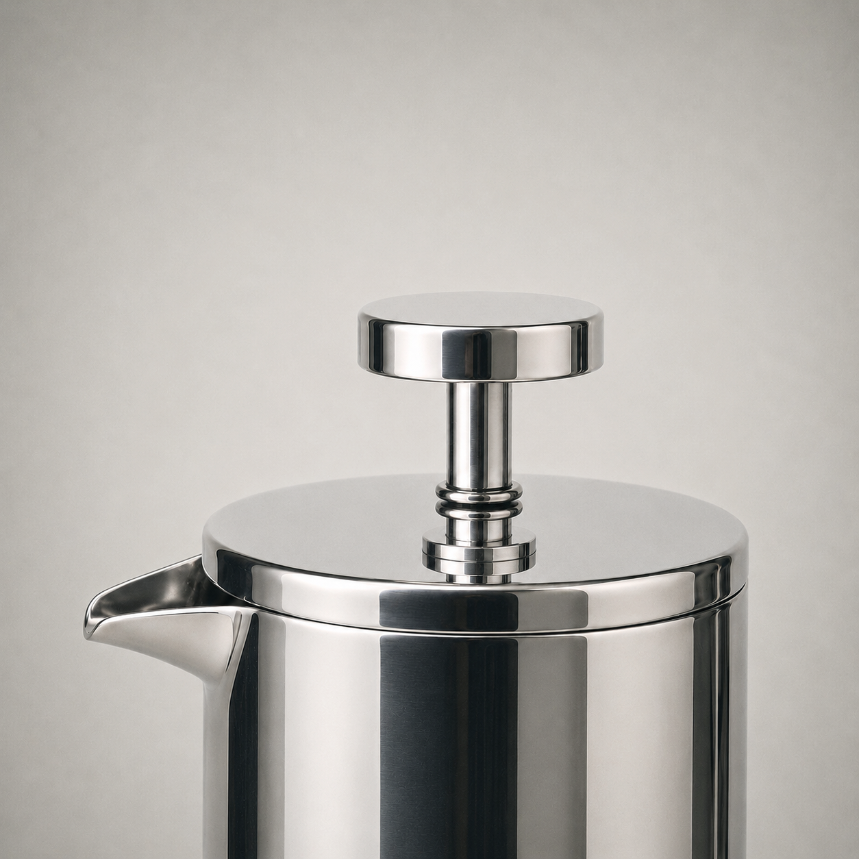 Close-up of the seated steel lid, the plunger rod and disc knob, and the pouring lip formed by the rim carried outward into an open trough