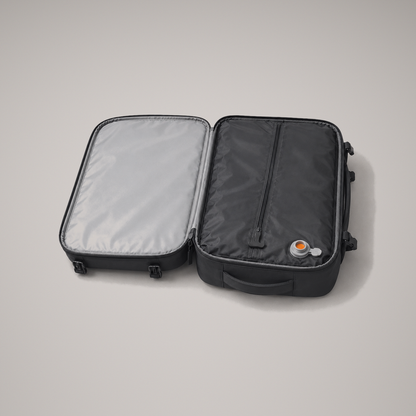 The backpack opened flat through 180 degrees on a grey studio background, showing the plain grey lined lid and the sealed black compression chamber with its single zip and grey air valve