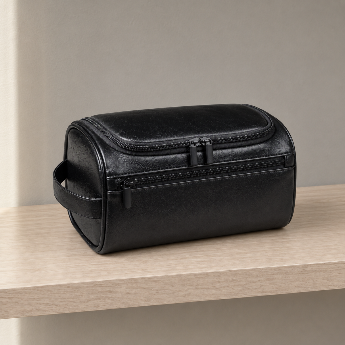 Black hanging toiletry bag closed on a wooden bathroom shelf, with black zip pulls and an end handle