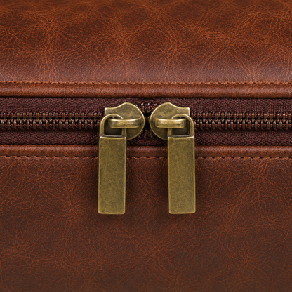 Close view of the two warm gold-toned zip sliders and flat pull tabs meeting on the top zip of the brown bag