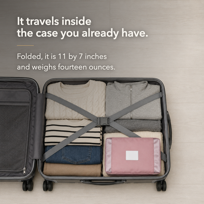 Pink travel bag folded flat and packed among clothes in an open suitcase, below the words It travels inside the case you already have