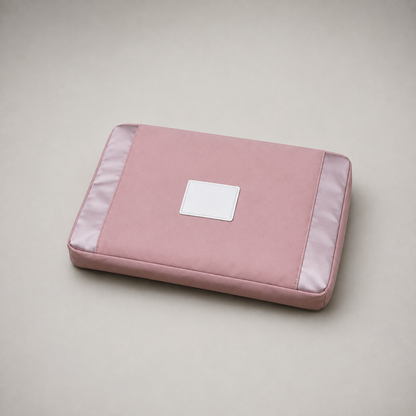 Pink travel bag folded flat into a rectangular pouch on a plain grey studio background, with a satin panel on each short end