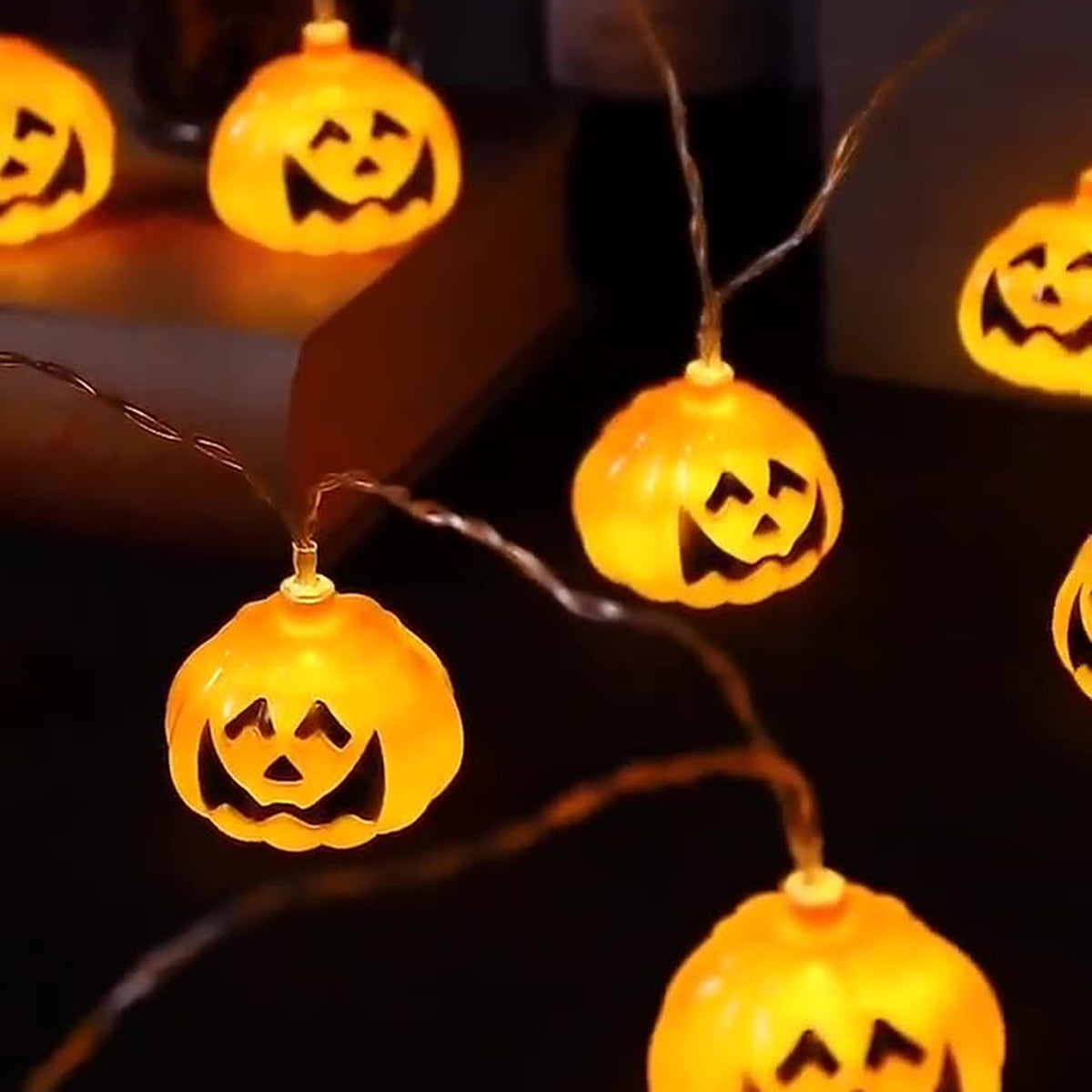 Pumpkin string lights lit warm white on a table at night, the carved faces clearly readable