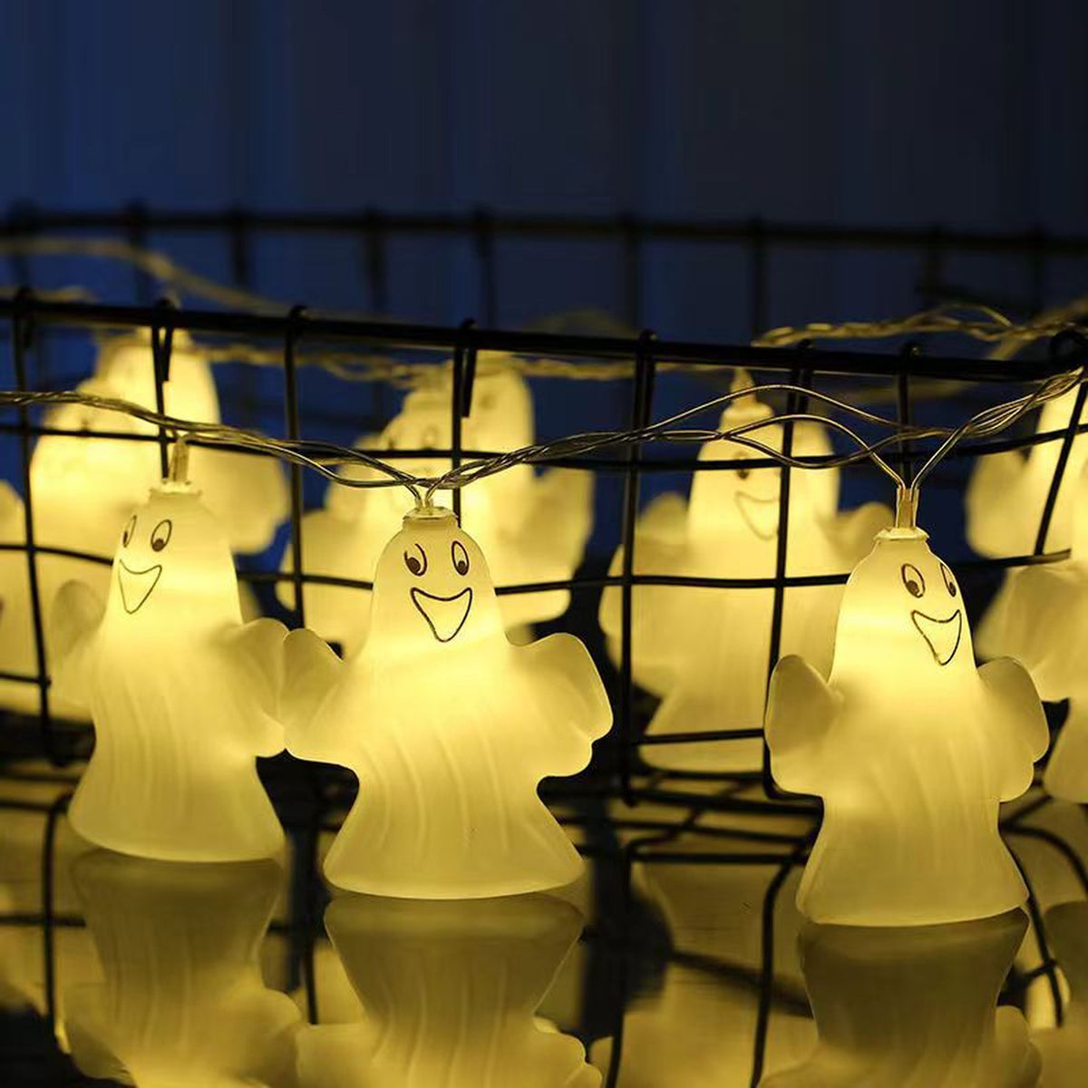 Ghost string lights lit along a black wire fence against a blue evening sky