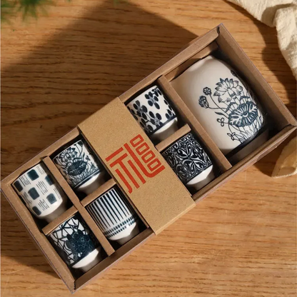 The sake set from above in its kraft box with a red-printed sleeve, on a wooden table beside a linen cloth.