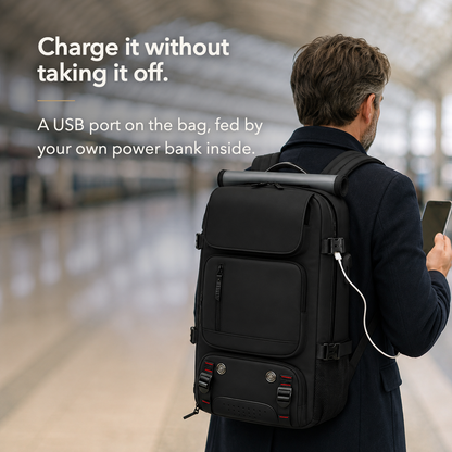 Man wearing the black backpack in a station, a white cable running from the USB socket on the bag's right side panel to the phone in his hand