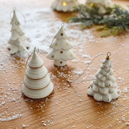 Four white ceramic tree ornaments standing upright on a wooden table scattered with artificial snow