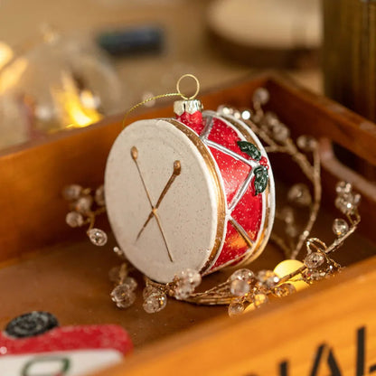 Close-up of the drum ornament with a cream head, crossed gold drumsticks, gold rims and holly on its red shell