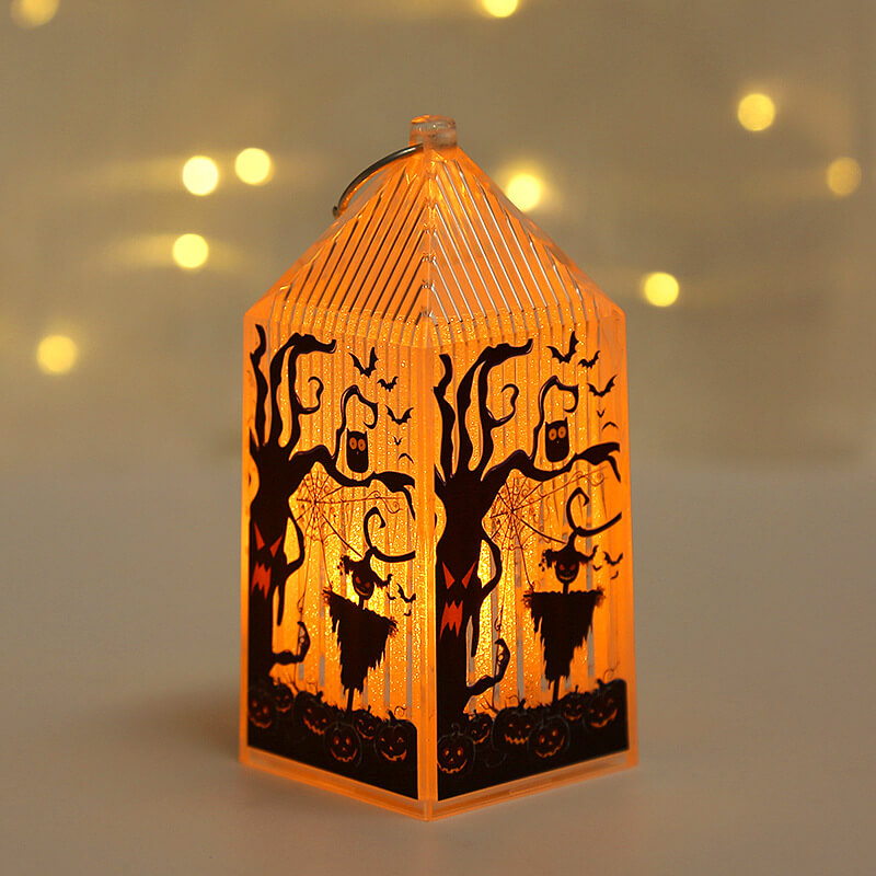 Mini Halloween lantern lit warm amber, printed with a gnarled tree face, an owl and a pumpkin-headed scarecrow