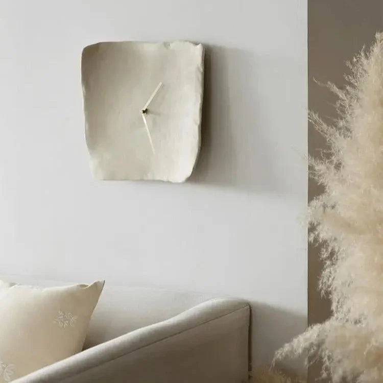 White crumpled resin wall clock hung above a gray sofa beside tall pampas grass