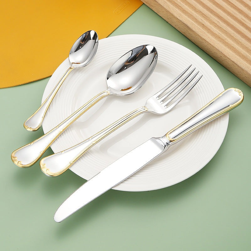 Gold-trimmed dinner knife, fork, spoon and teaspoon resting across a white plate