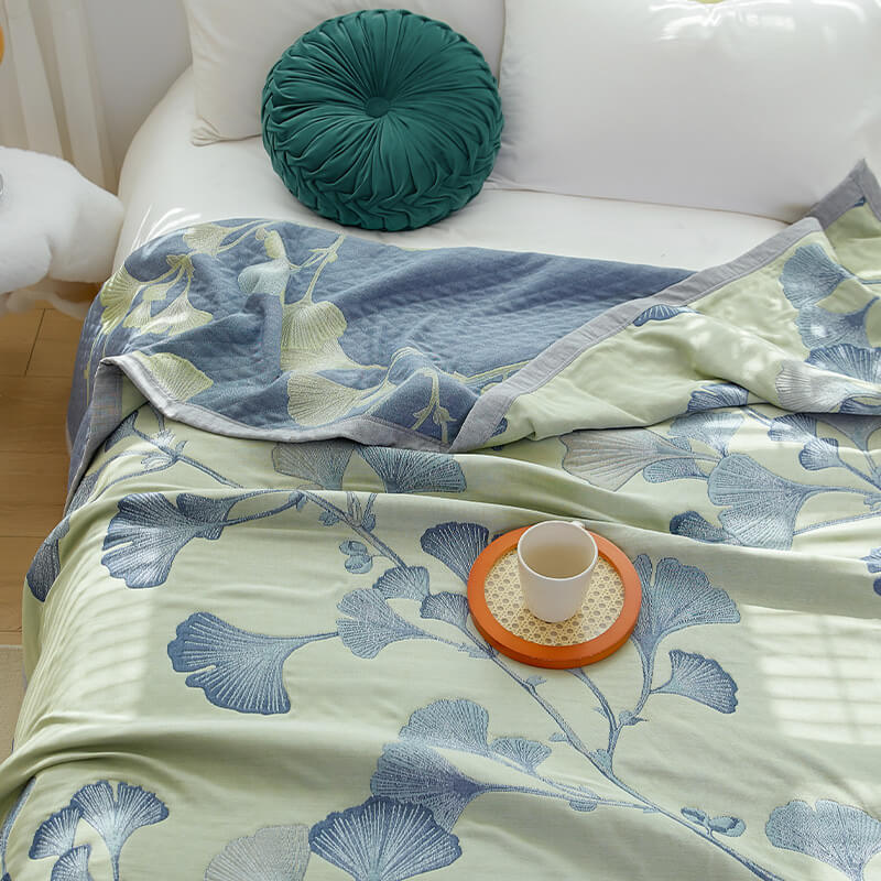 Green ginkgo leaf quilt on a white bed beside a round green cushion, its corner turned back to show the reverse