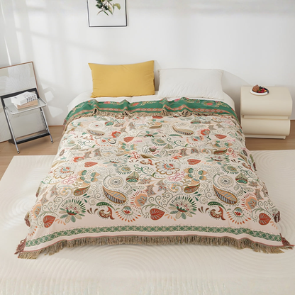 A cream throw blanket with rust and sage leaves and paisleys over a white bed, the top turned back to show its deep green reverse