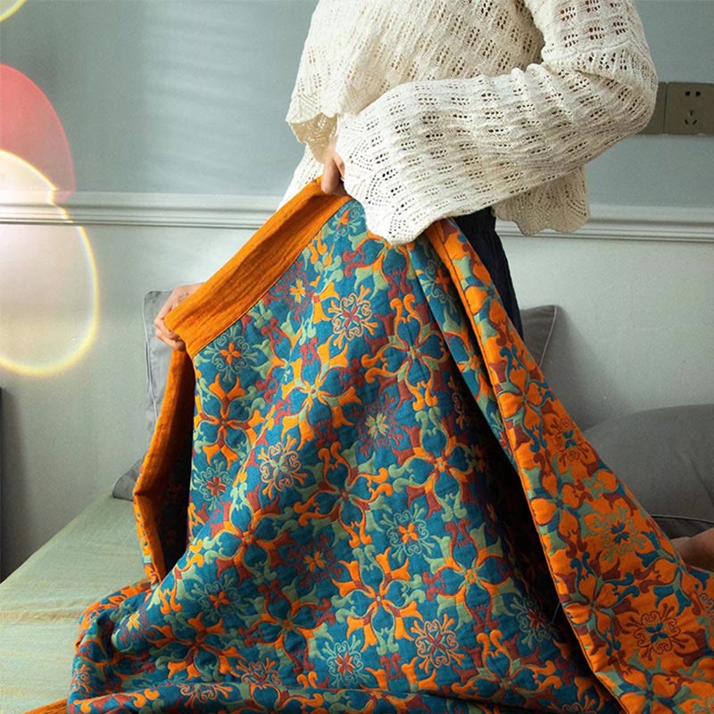 Hands lifting the cotton quilt to show its blue front, orange reverse and orange border