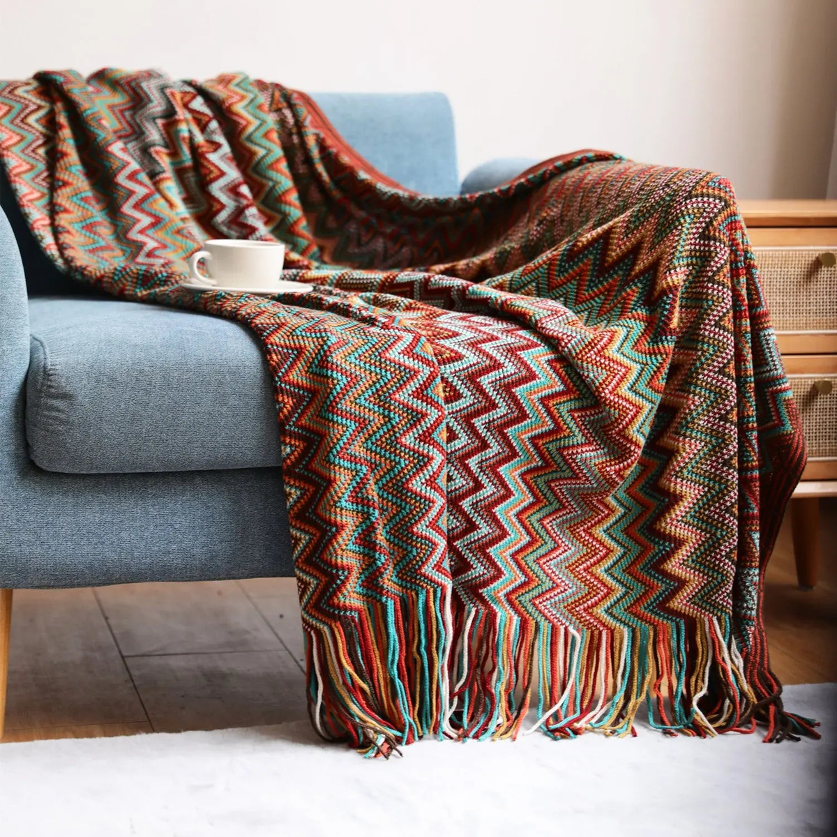 A red chevron throw with rust and turquoise zigzags spread across a blue couch beside a rattan cabinet.
