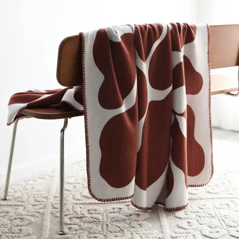 A rust and off-white knit throw blanket hung over a wooden bench, its stitched edges running down both sides.