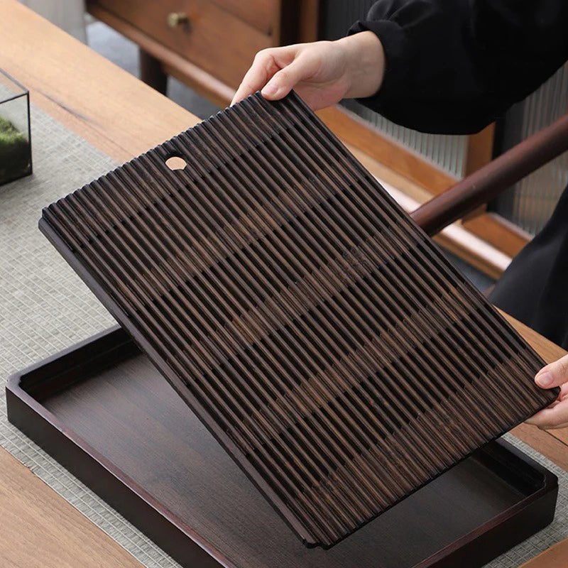 Two hands lifting the slatted top out of the tea tray, showing the empty reservoir box underneath.