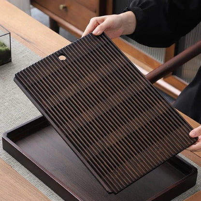 Two hands lifting the slatted top out of the tea tray, showing the empty reservoir box underneath.