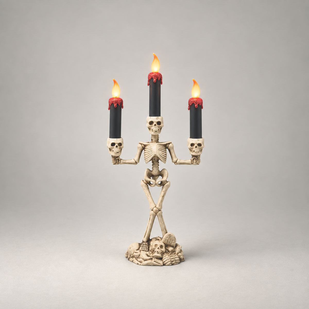 Halloween skeleton candle holder in red, three lit LED candles, on a plain grey studio background