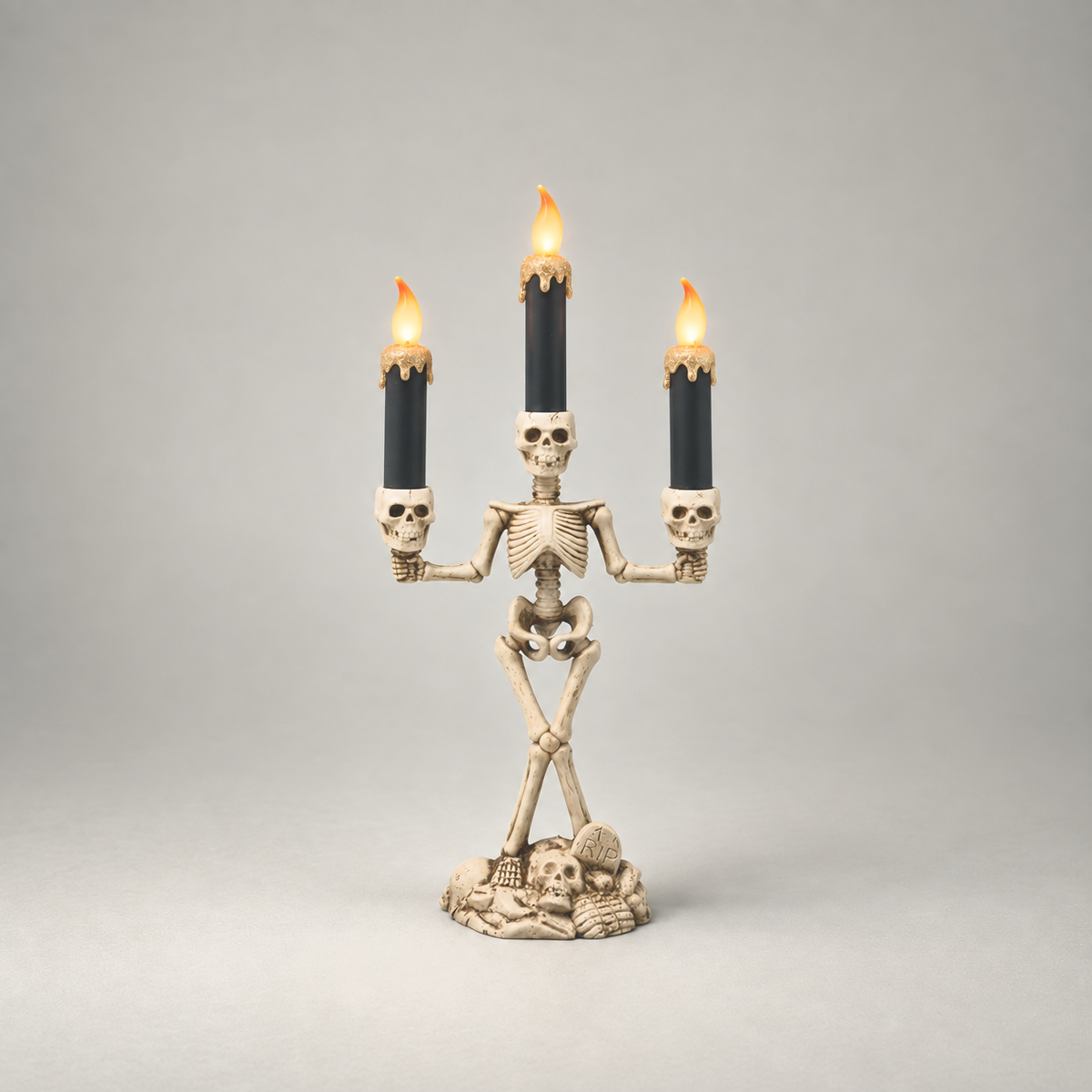 Halloween skeleton candle holder in gold, three lit LED candles, on a plain grey studio background