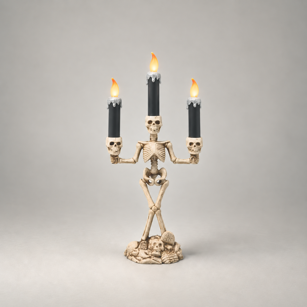 Halloween skeleton candle holder in silver, three lit LED candles, on a plain grey studio background