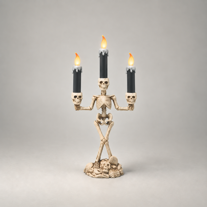Halloween skeleton candle holder in silver, three lit LED candles, on a plain grey studio background