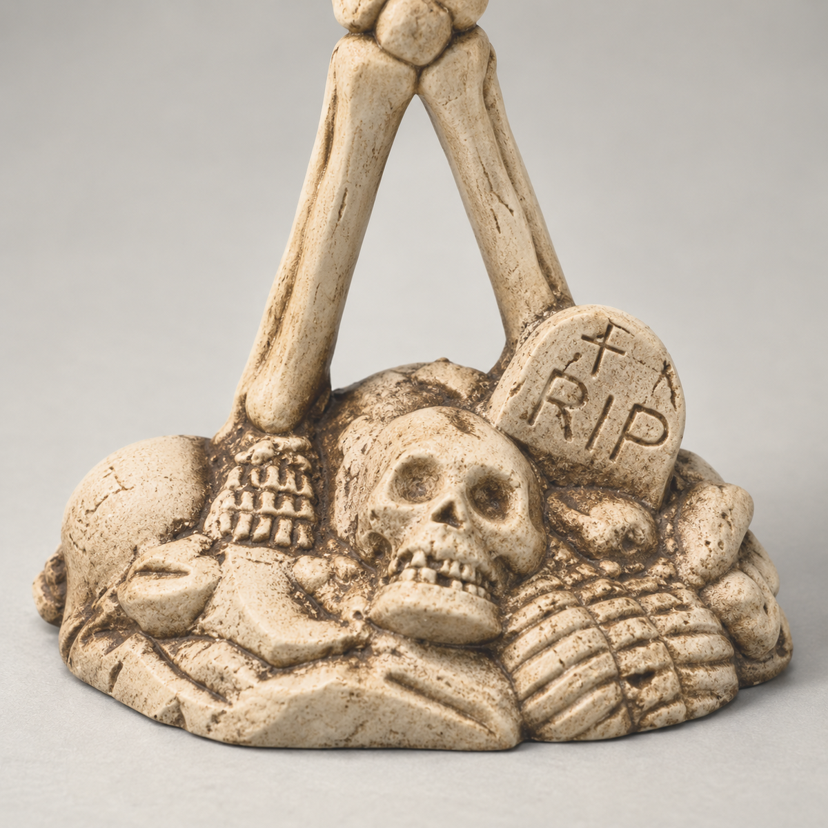Close-up of the skeleton candle holder's base, showing the sunken skull and the carved headstone