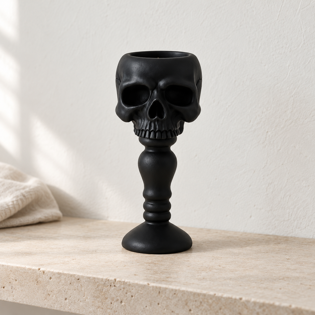 Black skull candle holder on a limestone shelf against pale plaster in daylight