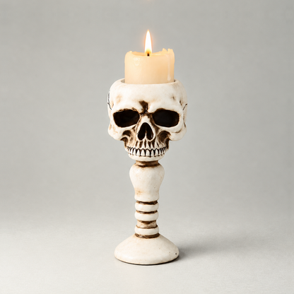 Bone skull candle holder shown front on against a plain grey studio background, with a short lit pillar candle standing in the well in the top of the head