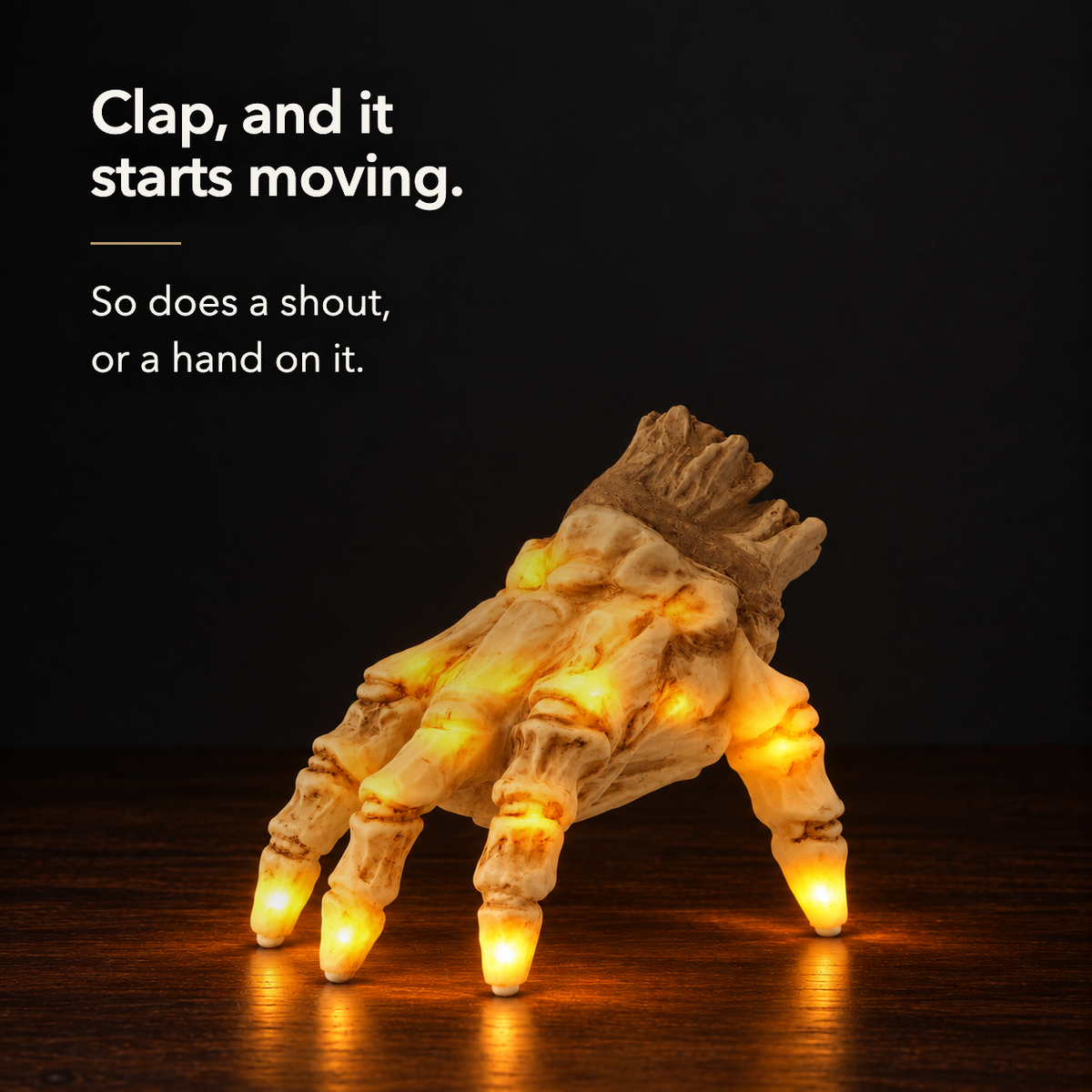 The lit skeleton hand glowing amber on a dark wood sideboard at night, lettered: clap, and it starts moving