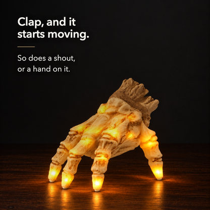 The lit skeleton hand glowing amber on a dark wood sideboard at night, lettered: clap, and it starts moving