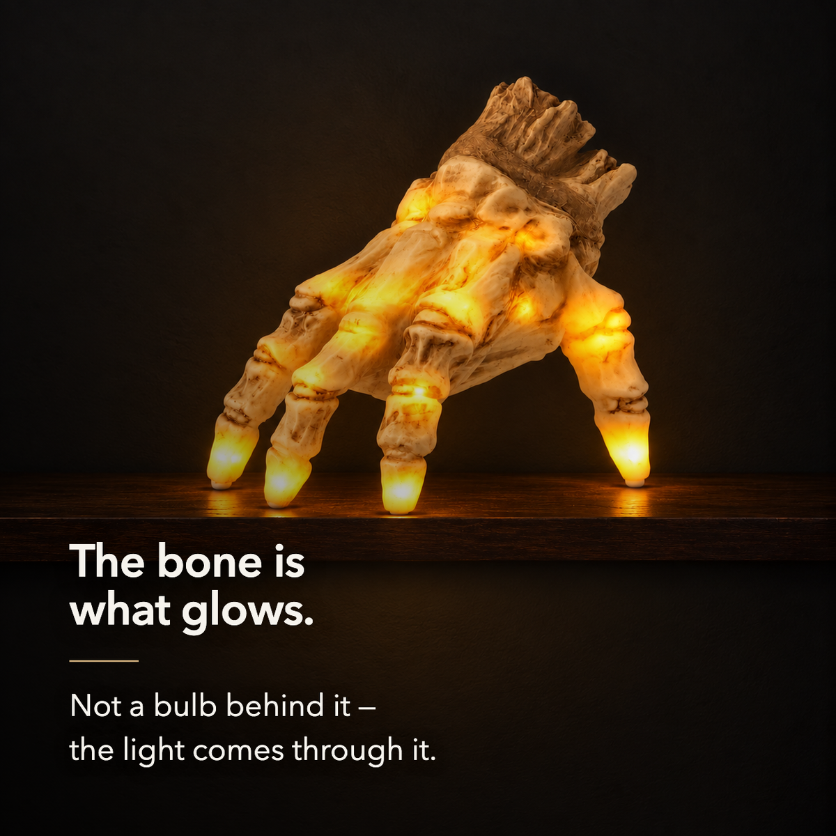The lit skeleton hand glowing on a dark wood mantel shelf at night, lettered: the bone is what glows