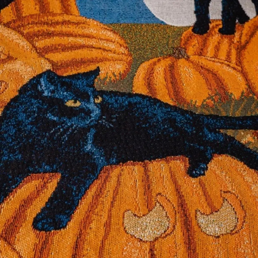 Close view of the woven design, a black cat with yellow eyes lying along a carved orange pumpkin under a pale moon, with a second cat standing above it