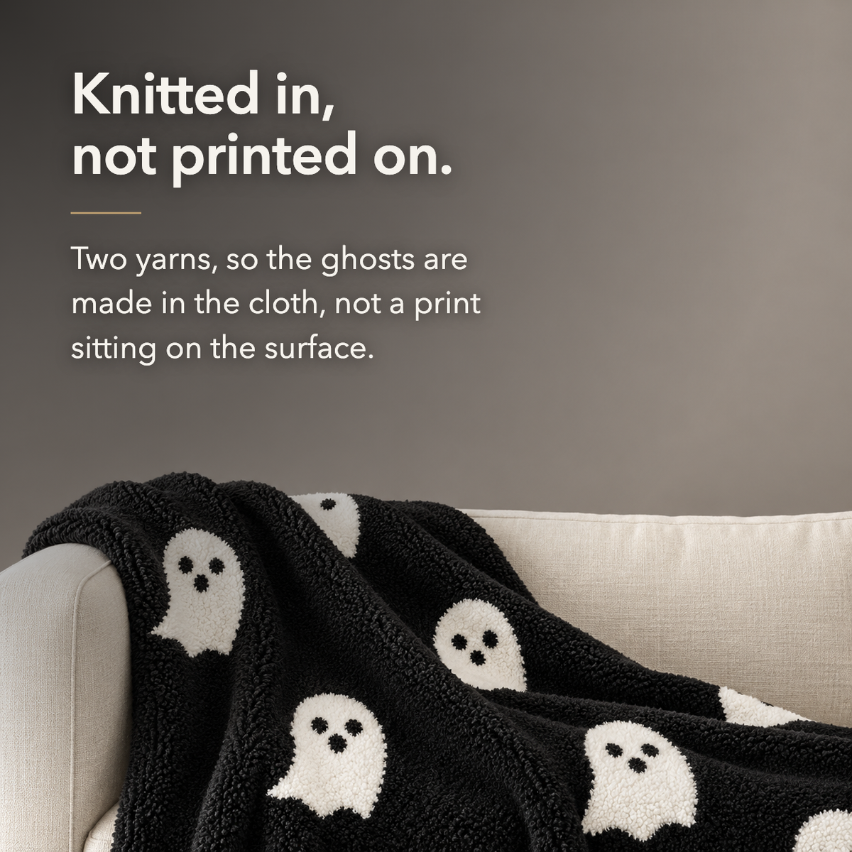 Black ghost knit throw blanket close up on a cream sofa, lettered with the words knitted in, not printed on