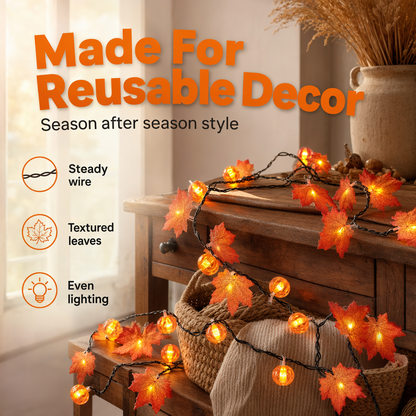 Maple leaf and pumpkin string lights lit and draped across a wooden console table beside a bright window