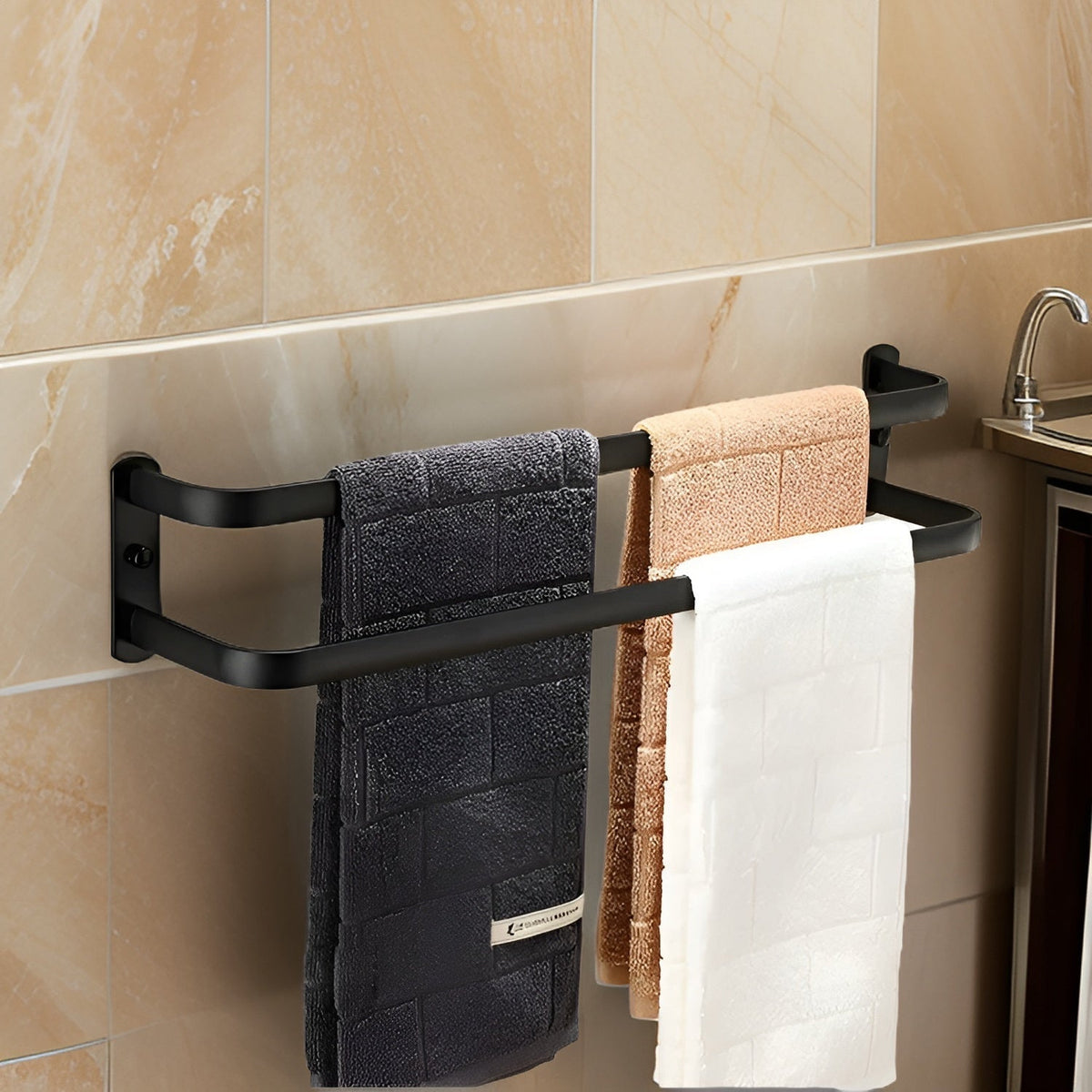 Two-bar matte black aluminum towel rack held to a beige marble bathroom wall by a plate at each end, with three hand towels on its stepped bars beside a basin