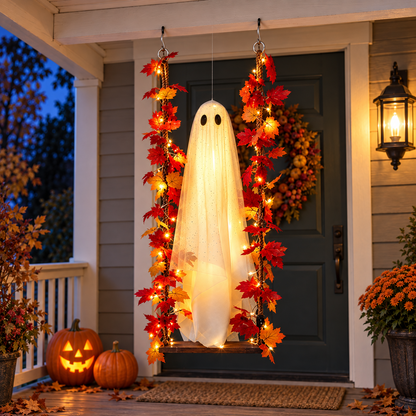 Glowing ghost swing hanging in front of a front door at dusk beside carved pumpkins