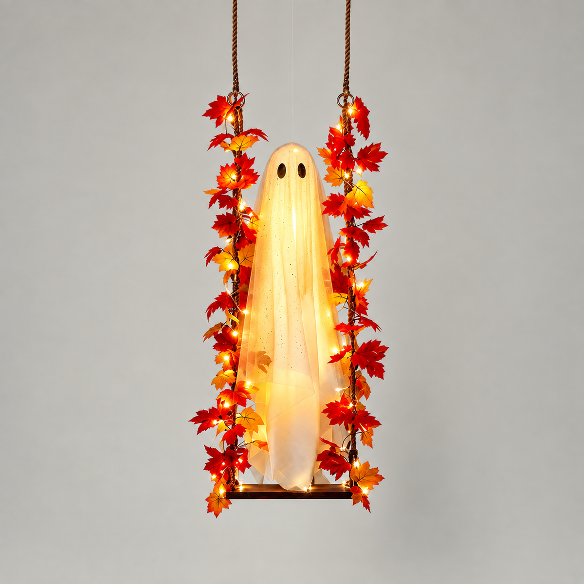 Hanging ghost swing with maple leaf garland and warm lights, lit, on a grey background