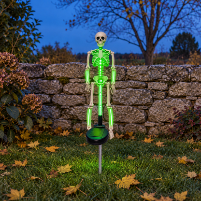 Green solar skeleton stake light glowing on a lawn in front of a stone wall at dusk