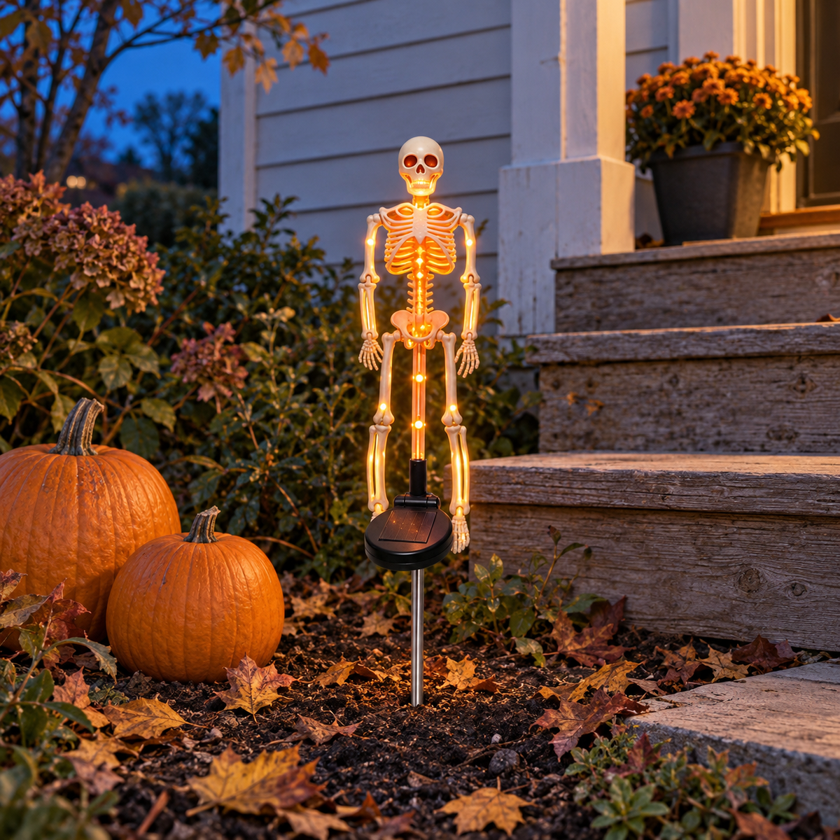 Orange solar skeleton stake light glowing beside two pumpkins at the foot of wooden steps at dusk
