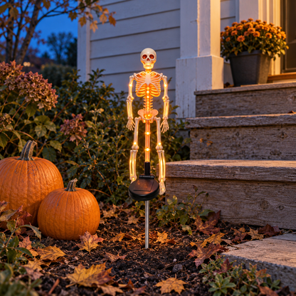 Orange solar skeleton stake light glowing beside two pumpkins at the foot of wooden steps at dusk