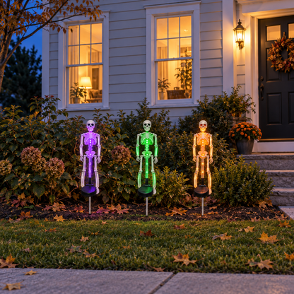 Purple, green and orange skeleton stake lights glowing in a front flowerbed, seen from the sidewalk in the evening
