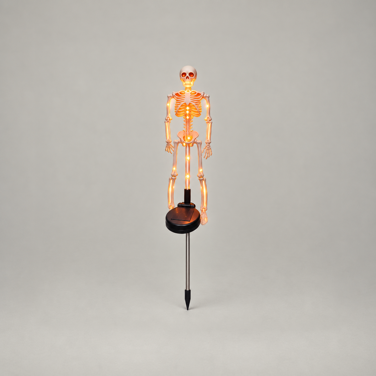 Orange solar skeleton stake light glowing, shown whole from skull to stake tip on a plain gray background