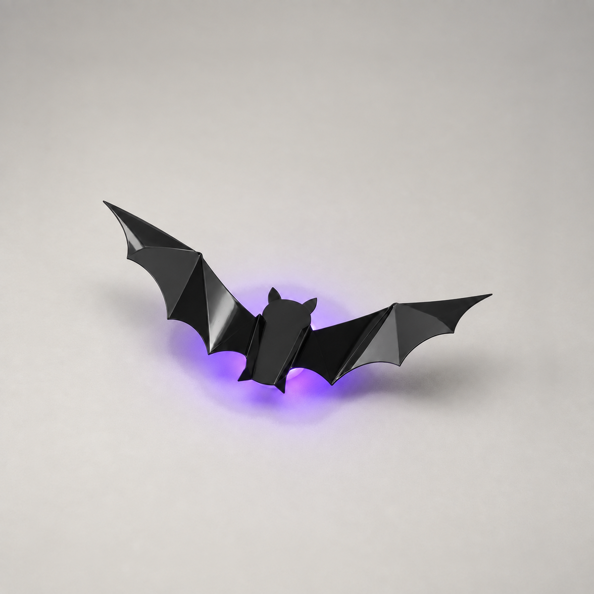One black PVC bat folded into a 3D shape on its round frosted LED light base, switched on
