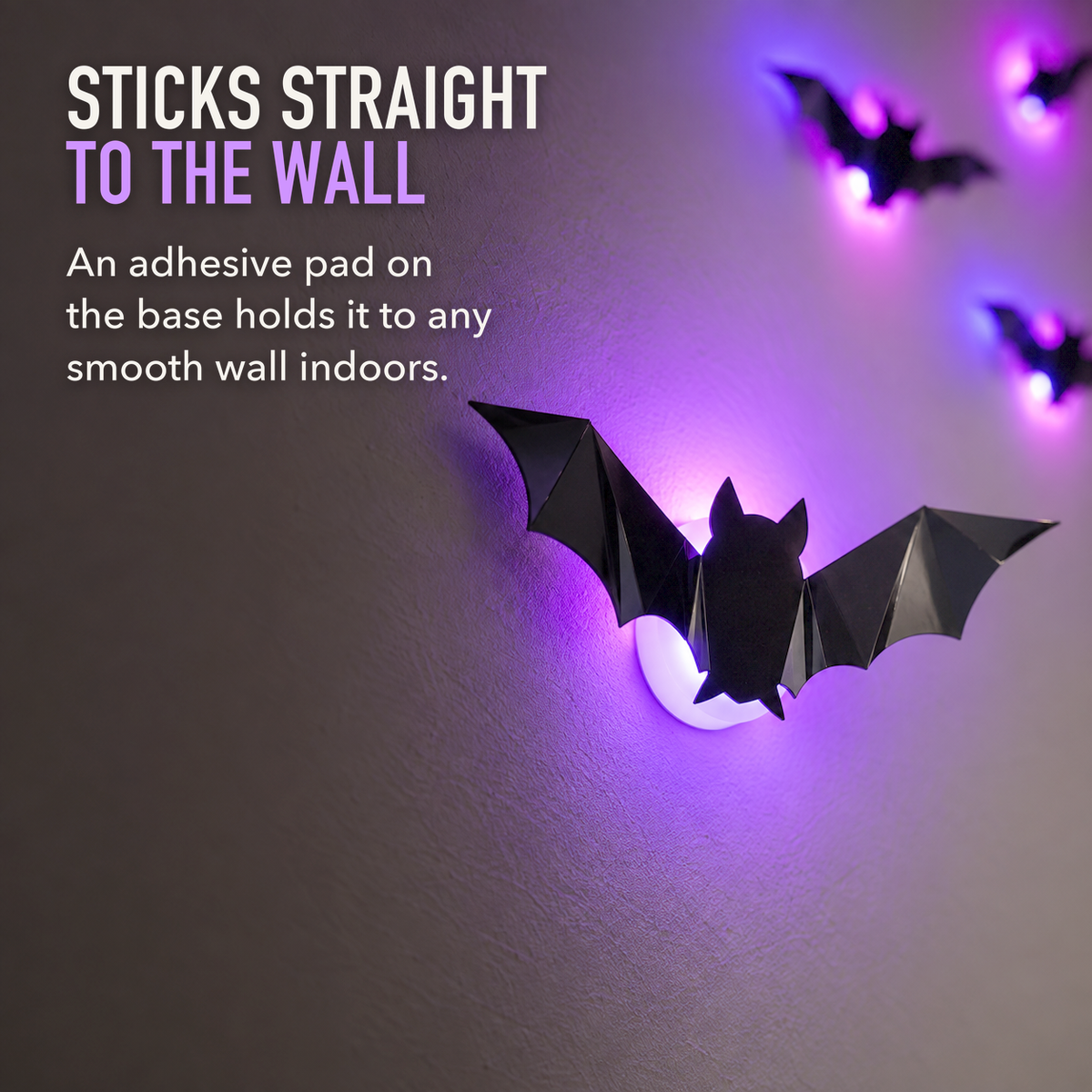Close-up of one black LED bat on its round frosted light base stuck to a wall, glowing purple, with the words Sticks Straight To The Wall